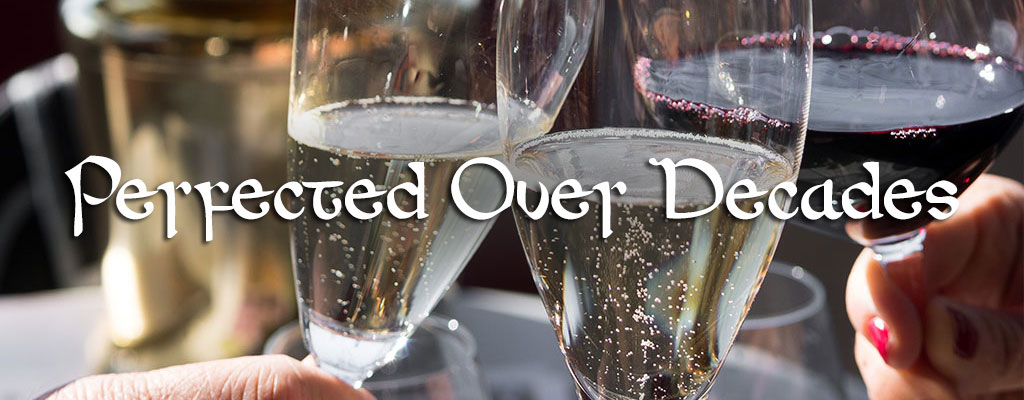 Close up view of 2 glasses of white wine and one red wine in celebrative toast with the words Perfected Over Decades in front